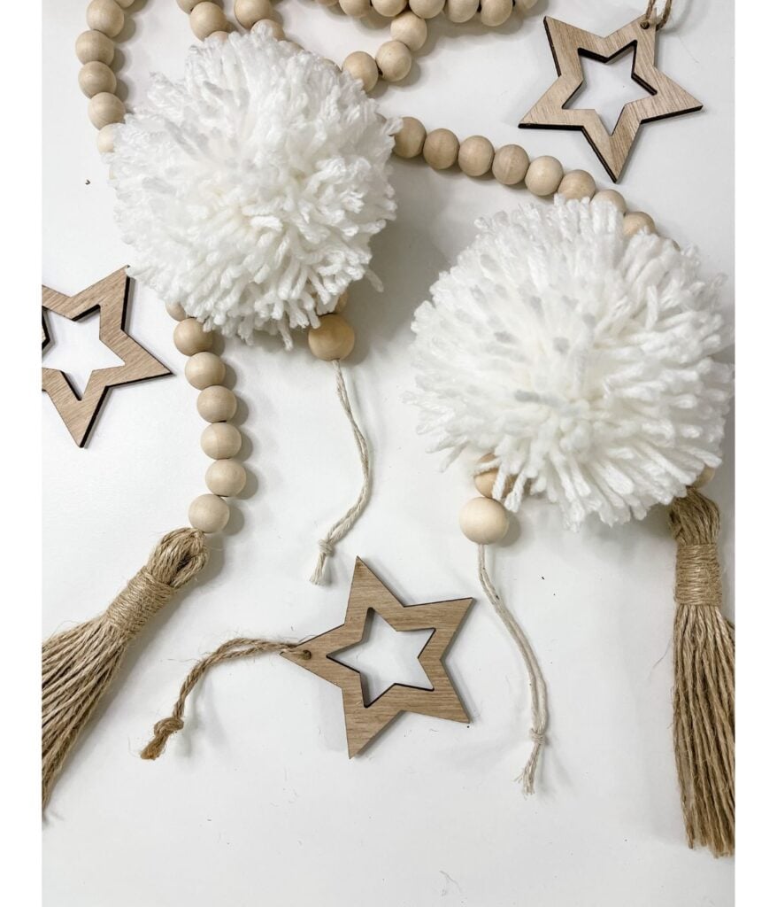 Boho Beaded Pompom decor featuring wooden beads, white yarn pom-poms, tassels, and wooden star ornaments arranged beautifully on a white surface.
