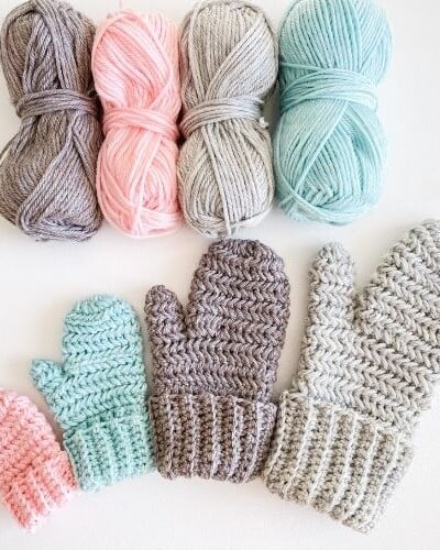 Herringbone crochet mittens and balls of yarn on a white surface.