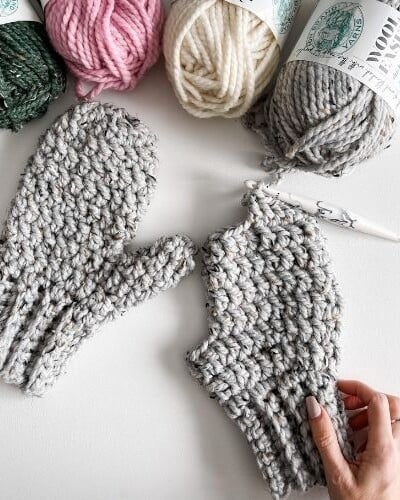 A beginner knitting mittens with bulky yarn in different colors.