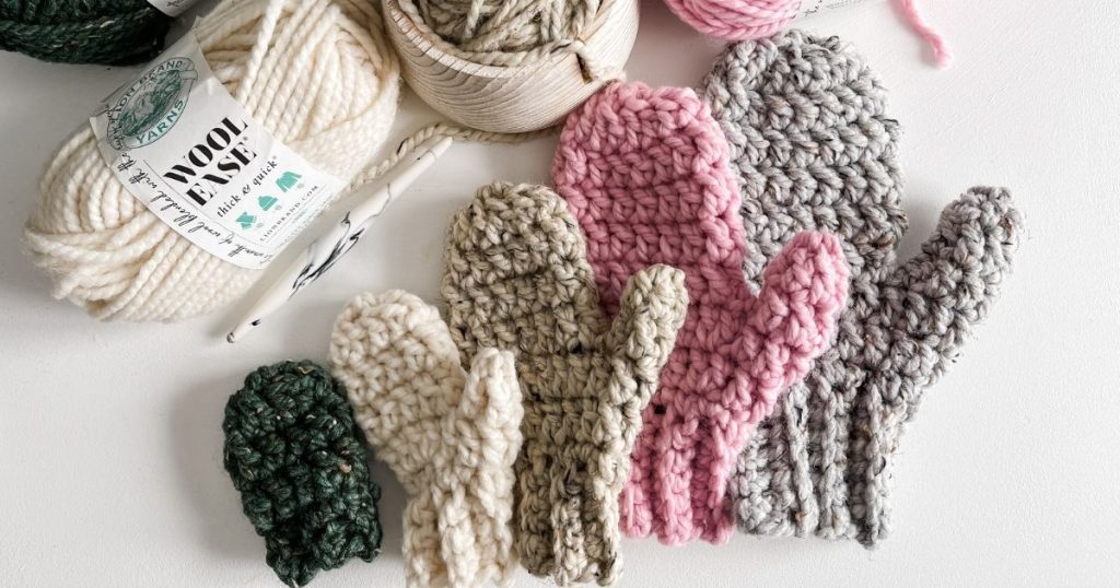 Beginner mittens, yarn, and knitting needles are laid out on a table.