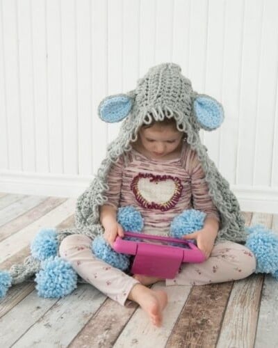 A little girl sitting on the floor with a sheep hoodie.