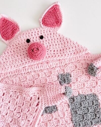 A pink crocheted pig hooded blanket with social media links.