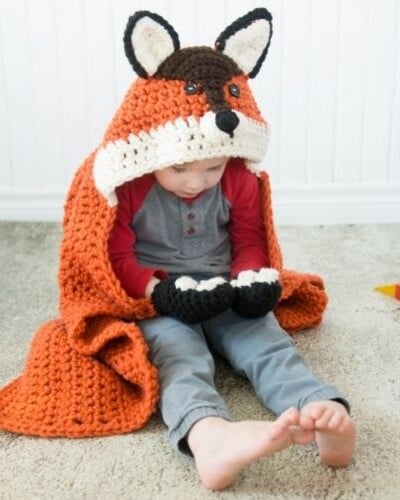 A little boy sitting on the floor with a hooded fox blanket.