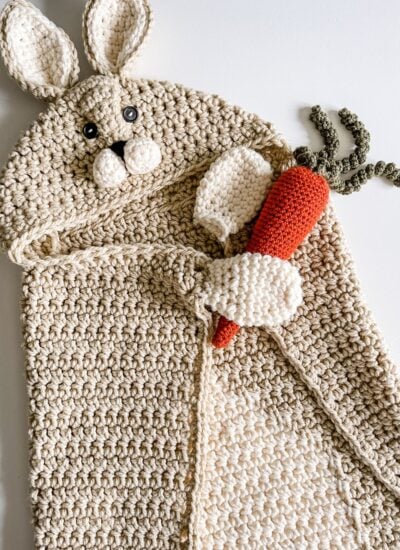 Handmade crochet hooded baby blanket with attached rabbit plush and carrot toy.