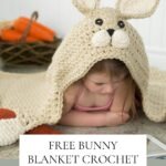 Little girl covered with a crochet bunny blanket featuring long ears and a cute face.