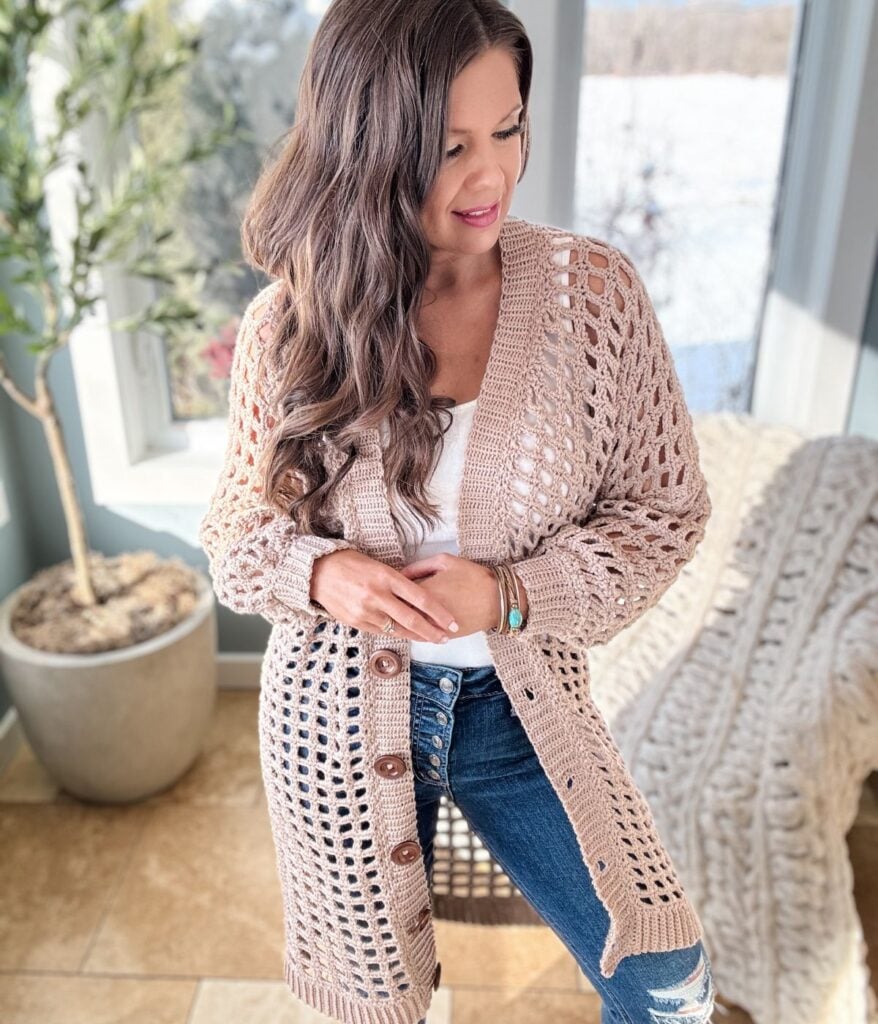 Woman in a beige crochet cardigan standing indoors.