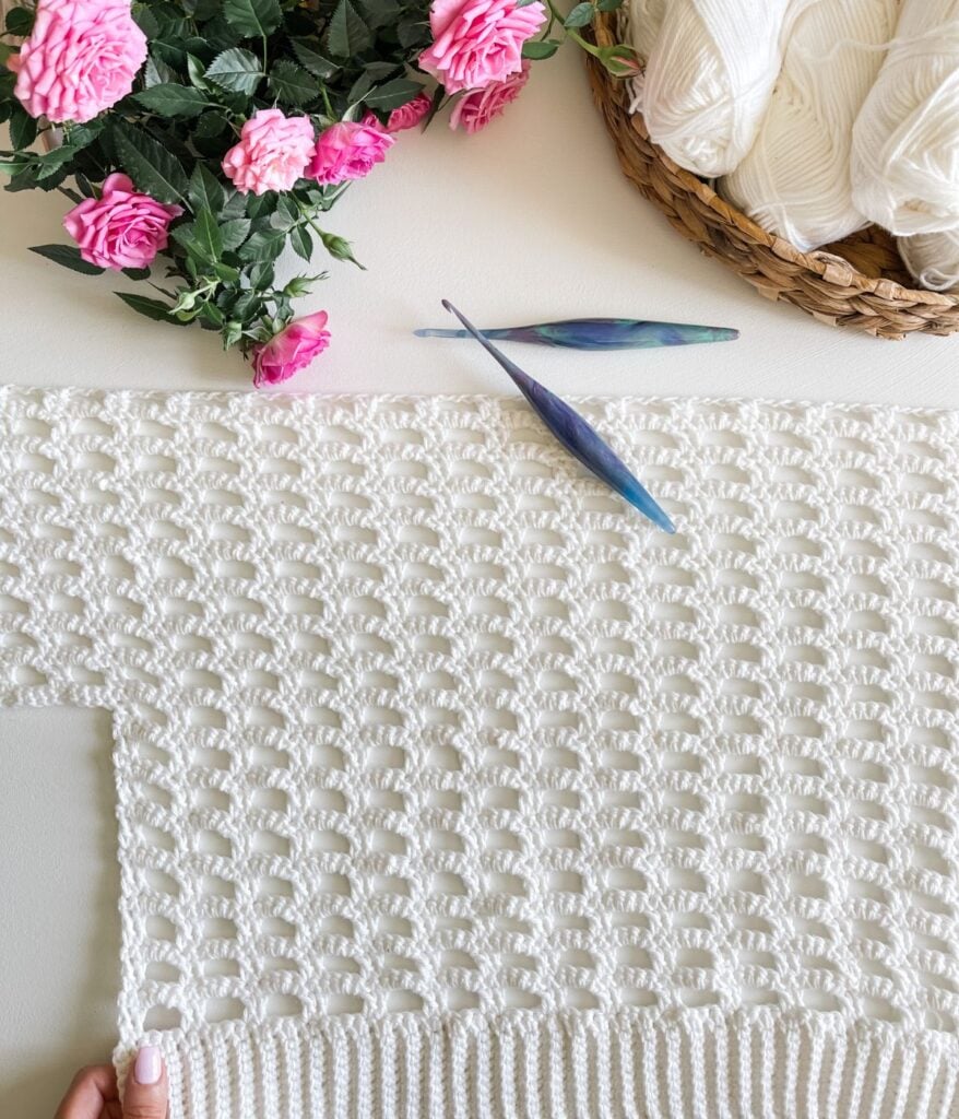Handmade crochet cardigan project with floral decoration and crochet hook.