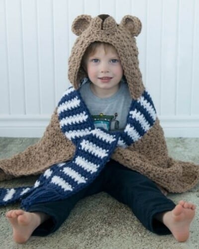 A young boy wearing a hooded bear blanket.