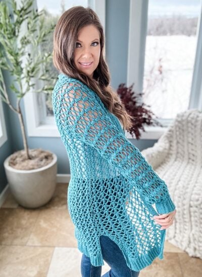 Woman posing in a blue crochet Cabot Trail cardigan indoors with a natural light background.