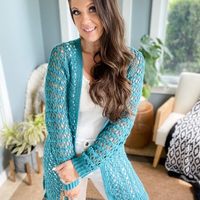 Woman in a turquoise Crochet Cabot Trail Cardigan posing in a room with plants and furniture.
