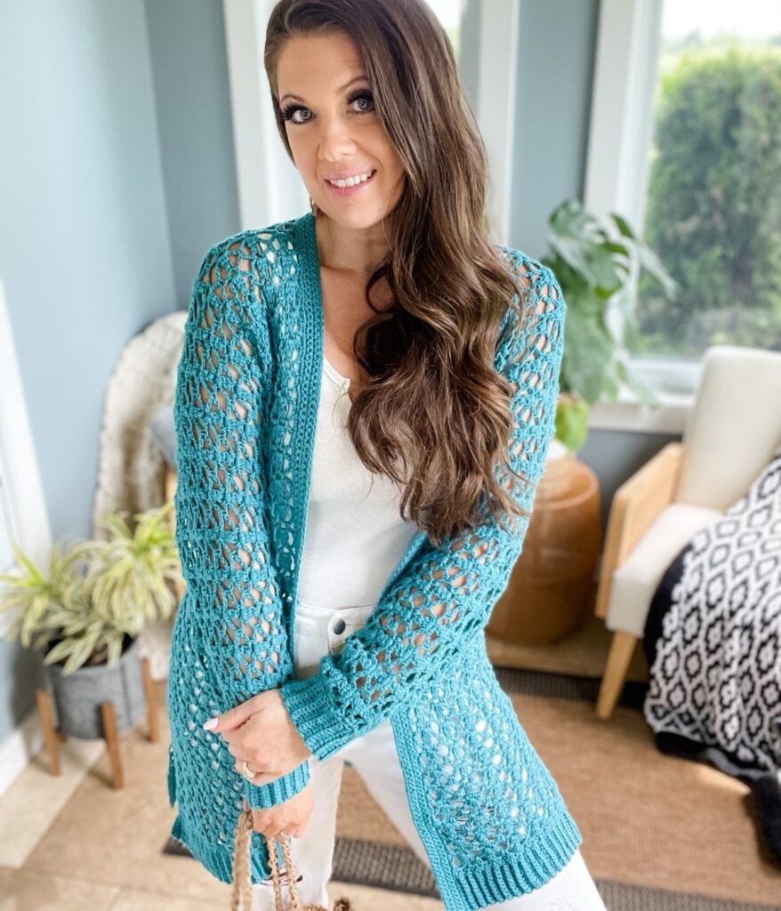 Woman in a turquoise Crochet Cabot Trail Cardigan posing in a room with plants and furniture.