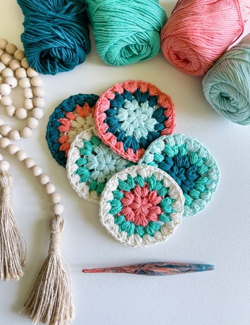 A group of crocheted coasters with yarn and tassels on a table.