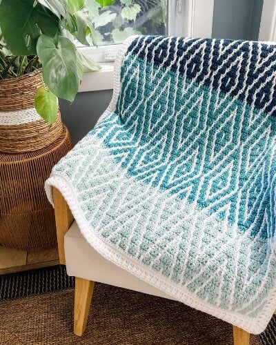 A Glistening Glacier Afghan sitting on a chair next to a potted plant.