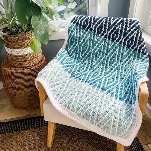 A Glistening Glacier Afghan sitting on a chair next to a potted plant.