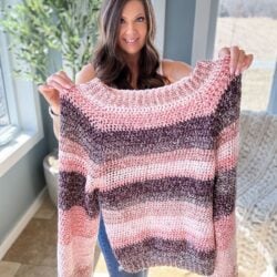 A woman smiling and holding up a hand-crocheted raglan sweater.