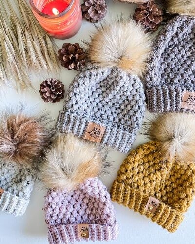Four knitted hats with pom poms and pine cones, including a puff stitch crochet hat.