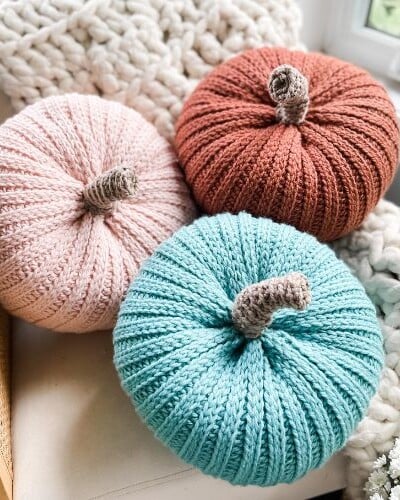 Three knit pumpkins sitting on a chair next to a window.