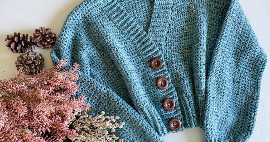 A lakeside blue crocheted cardigan with buttons and pine cones.