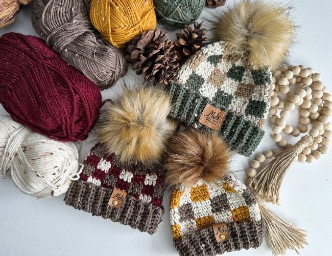 Rustic crocheted hats with pom poms and yarn featuring a buffalo plaid design.