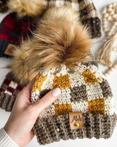 A hand holding a rustic crocheted hat with a pom pom.