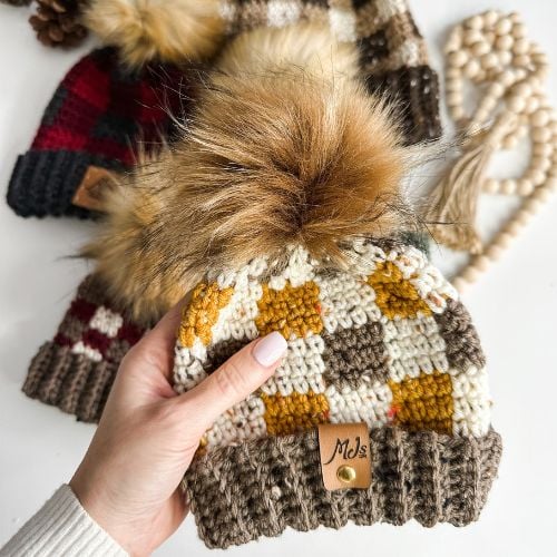 A hand holding a rustic crocheted hat with a pom pom.
