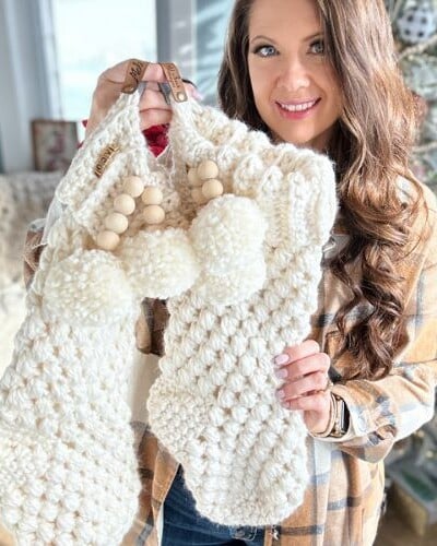 A woman holding up a bulky crochet stocking with pom poms.