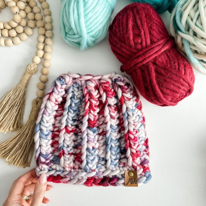 A person is knitting a Messy Bun Beanie with yarn on a table.