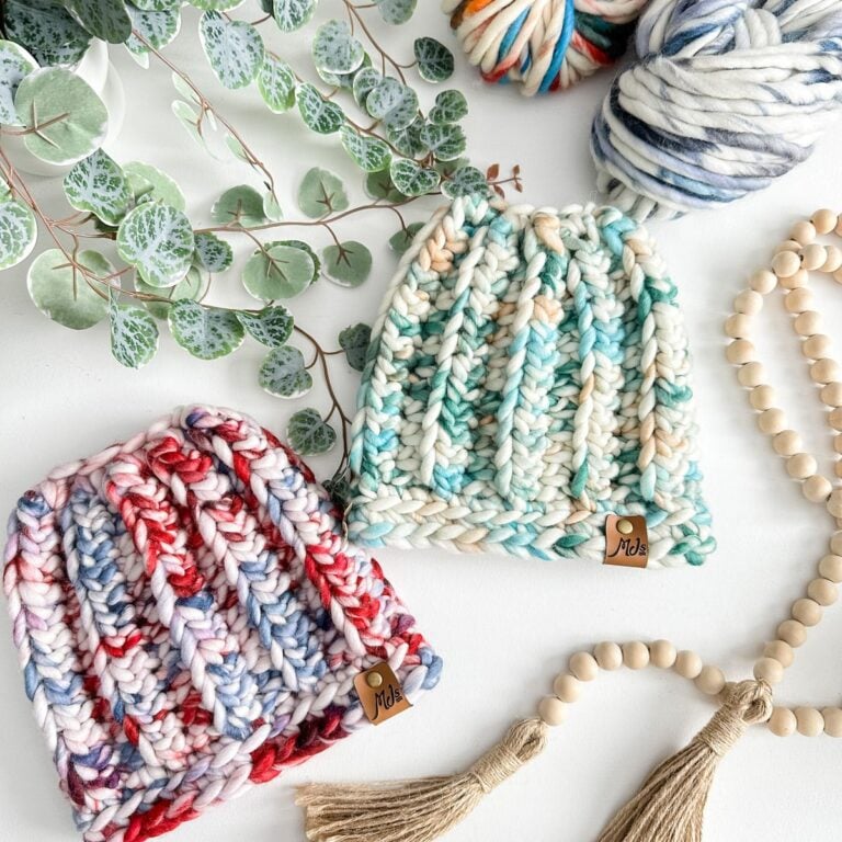 Two Messy Bun Beanies on a table with yarn and tassels.