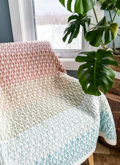 A beautiful mosaic crochet blanket sitting on a chair next to a potted plant.