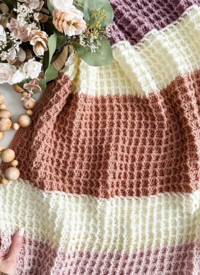 A hand holding a waffle stitch blanket on a white table.