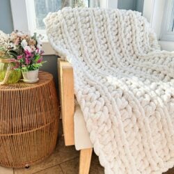 A white chunky throw blanket on a chair in front of a window.