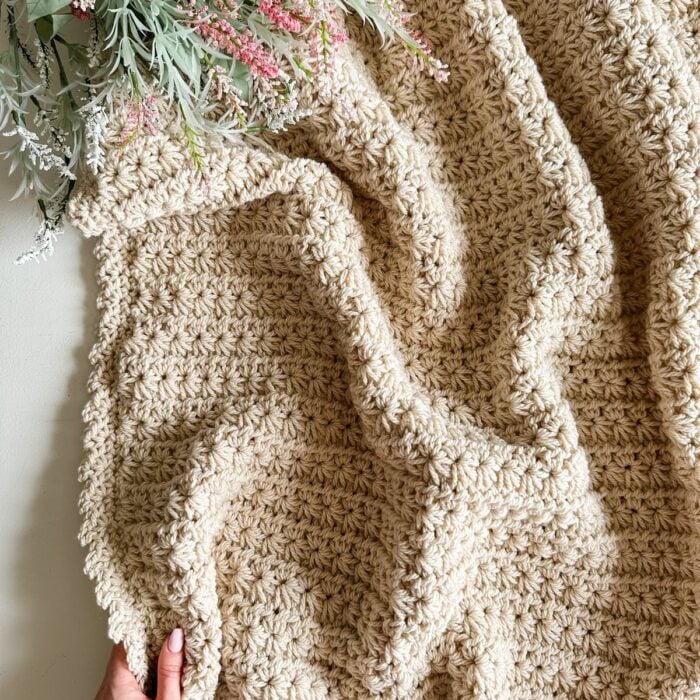 A person holding a crocheted Star Stitch blanket on top of a table.