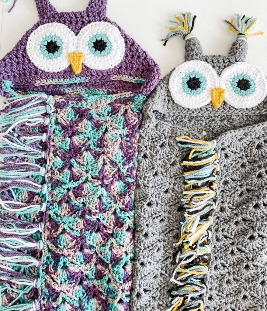 Two crochet hooded owl blankets—one in purple and blue, the other in gray and yellow—feature large eyes, beaks, and playful tassel details for a cozy and whimsical touch.