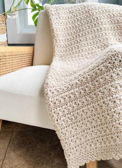 A Star Stitch crochet blanket sitting on a chair next to a potted plant.