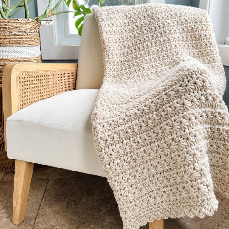 A Star Stitch crochet blanket sitting on a chair next to a potted plant.