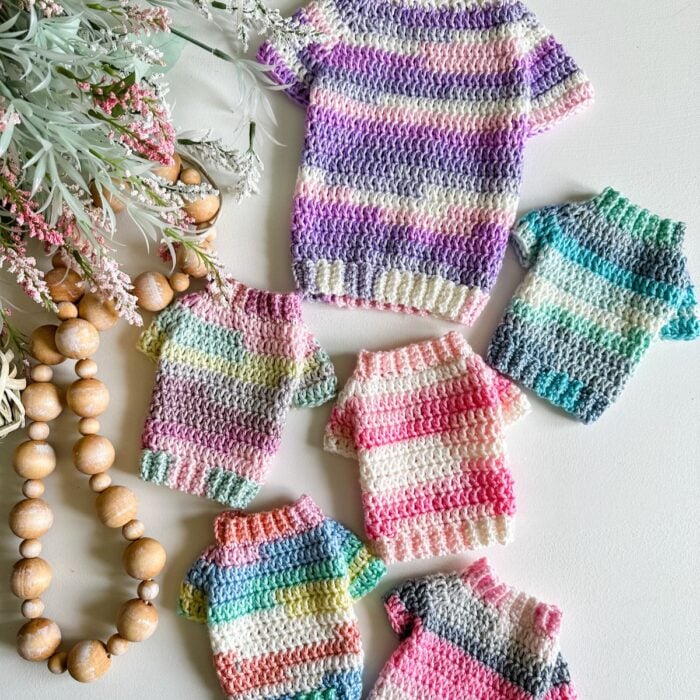 A small group of knitted sweaters with a crochet pattern for cats on a table.
