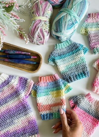 Crocheted sweaters and crochet needles on a table, featuring a crochet pattern for cats.