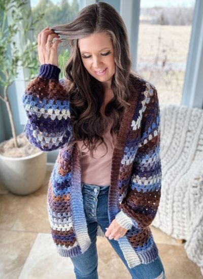 A woman in a Granny Stitch cardigan with a pink top underneath, running her fingers through her hair.