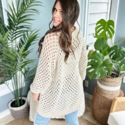 A woman wearing a beige granny stitch cardigan and jeans.