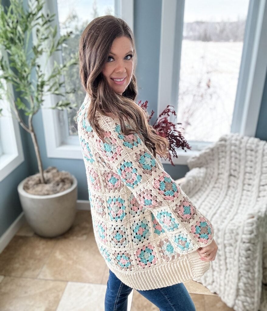 Woman in a Granny Stitch Cardigan posing with a smile by a window.