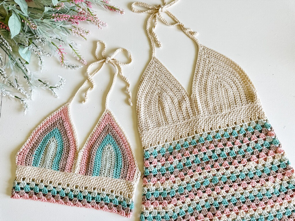 Two crocheted bikinis on a table next to flowers, showcasing the exquisite craftsmanship of Mjs Off The Hook Designs.