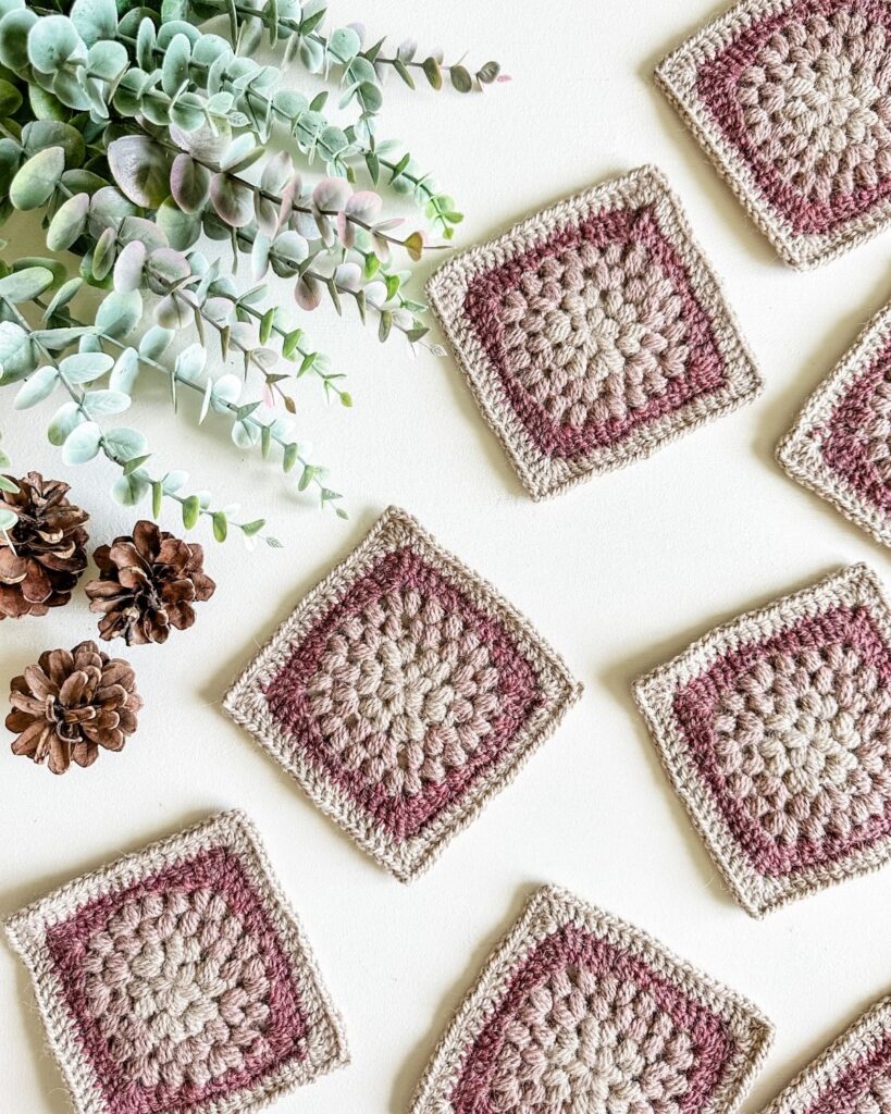 A set of crocheted granny squares surrounded by pine cones.
