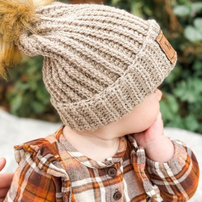 A baby wearing a beanie with a crochet pom pom.