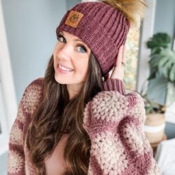 A woman wearing a burgundy Rocky Ridge crochet hat with a pom pom.