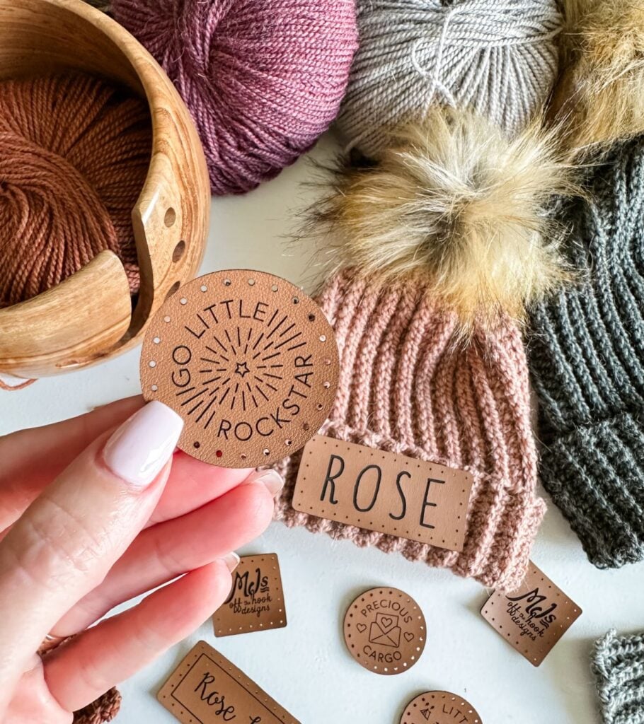 A person is holding a knitting hat with a sticker on it and a crochet bag.