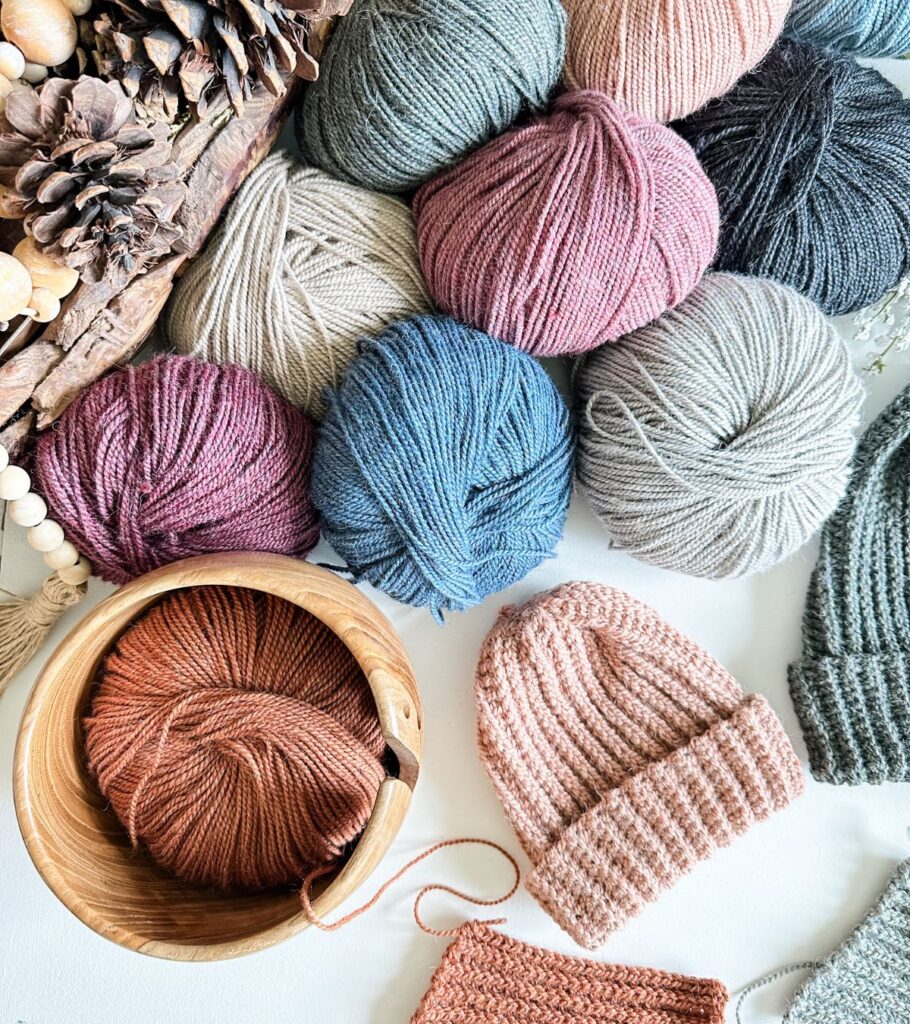 A colorful assortment of yarns and hats displayed on a white table, perfect for any crochet enthusiast or someone in need of a stylish hat.