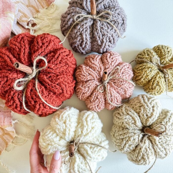 Four crochet pumpkins on a table with a hand holding them.