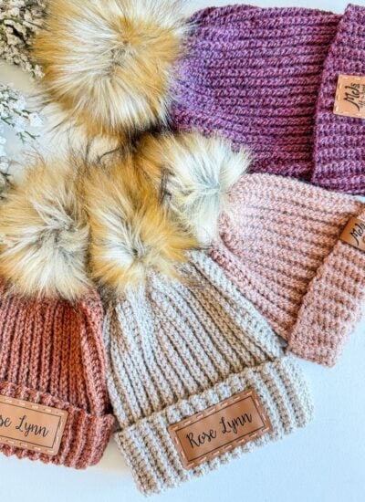 Four crochet hats with pom poms on them.