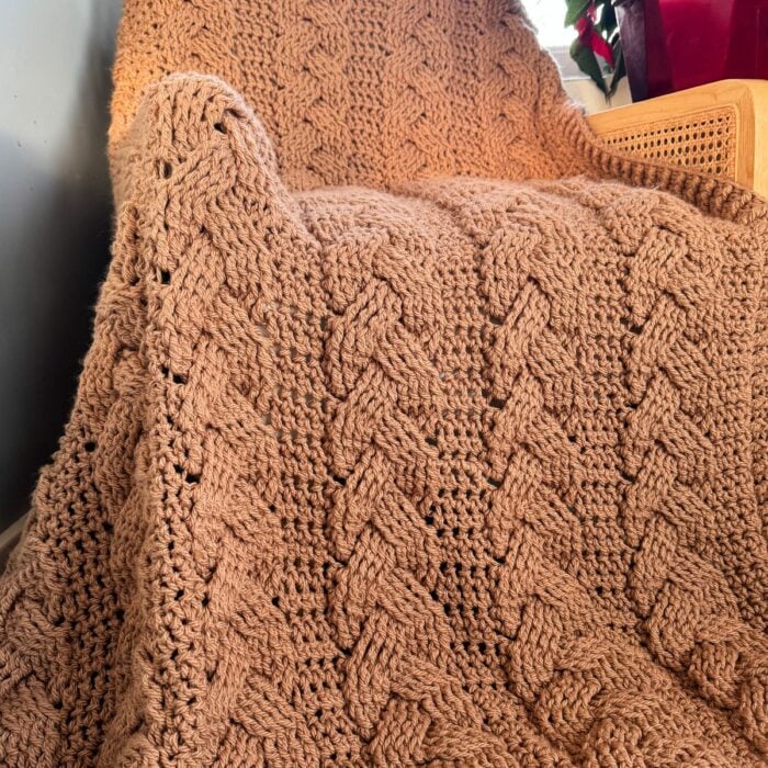 A cabled throw blanket sitting on a chair next to a potted plant.