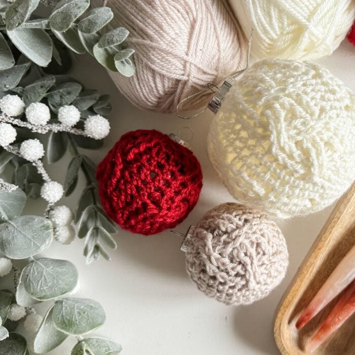 A group of crocheted Christmas ornaments and eucalyptus leaves on a white surface.